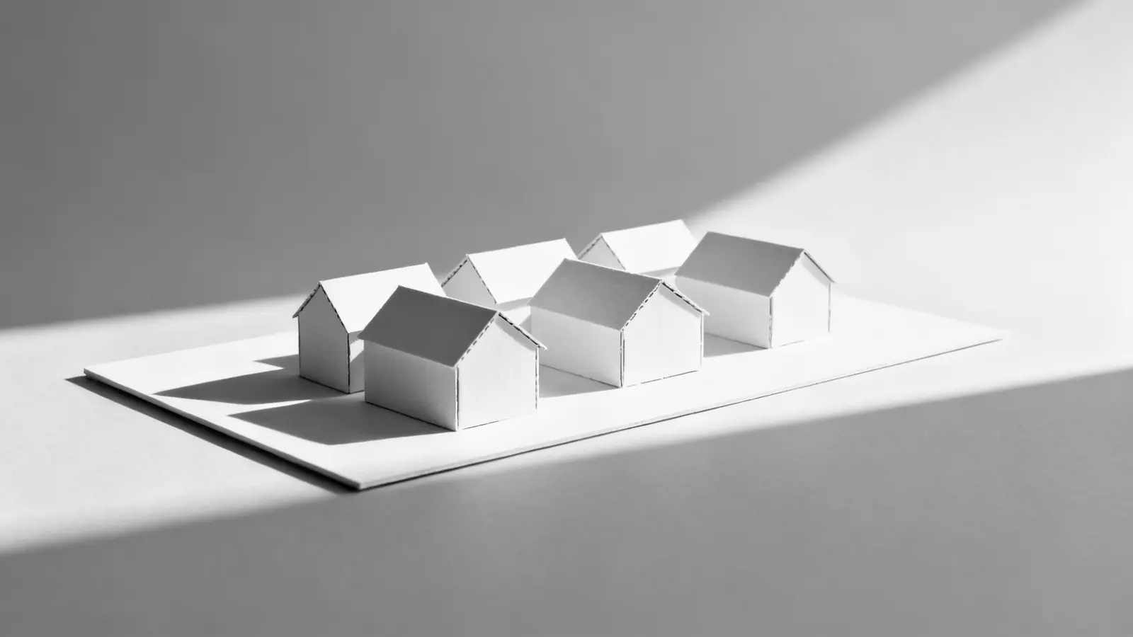 Weißes Arbeitsmodell aus Karton mit fünf Baukörpern auf einer Grundplatte im Streiflicht